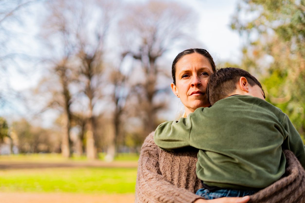 A woman in the park holding her toddler son with a serious expression on her face
